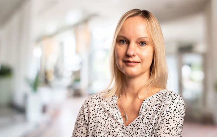 Eine junge, lächelnde, blonde Frau in einem hellen und sommerlichen Oberteil.