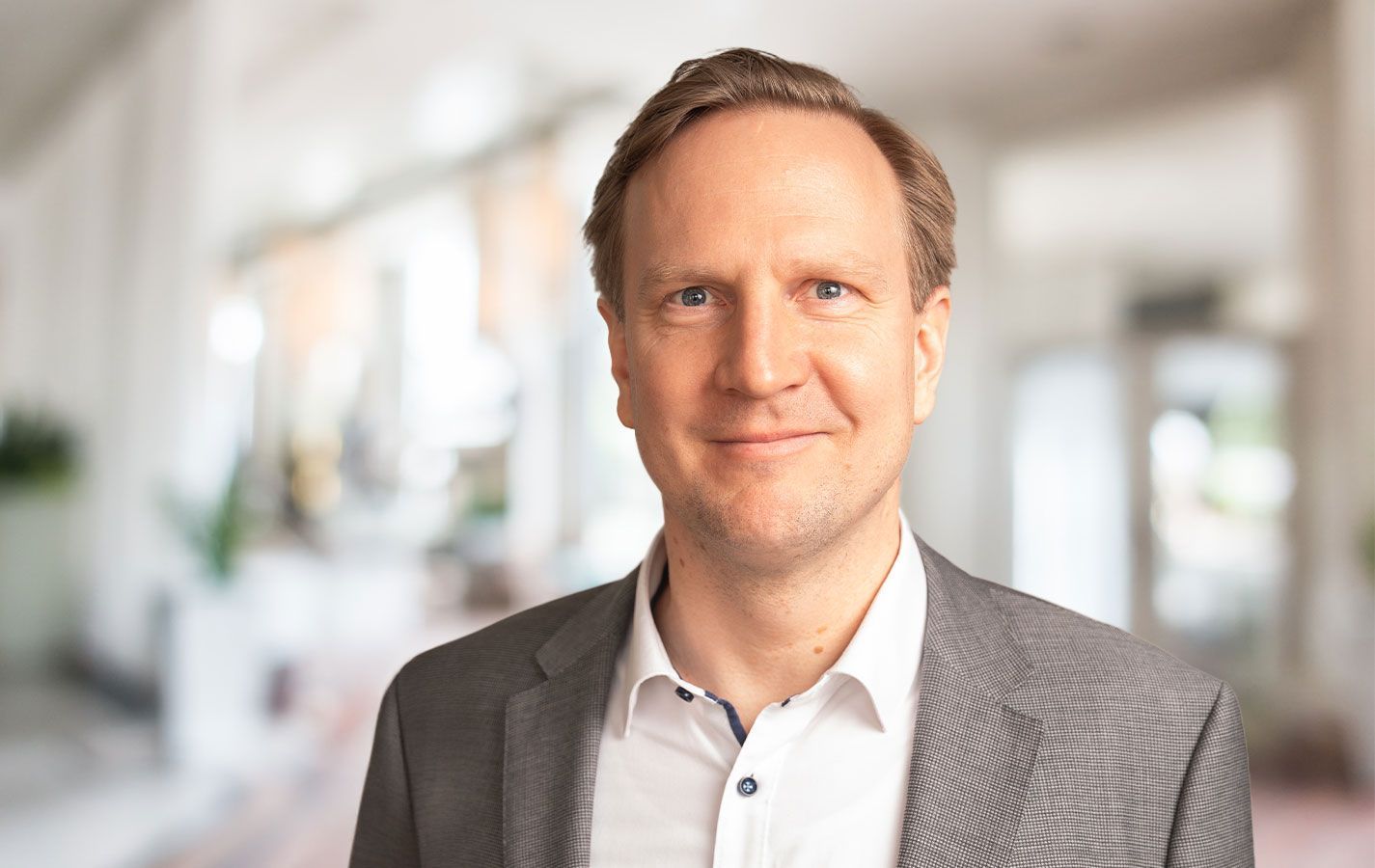 Freundliches Porträt von David Kopka, Ansprechpartner im Außendienst. Lächelnder Mann im Anzug, in einem modernen Büroambiente.