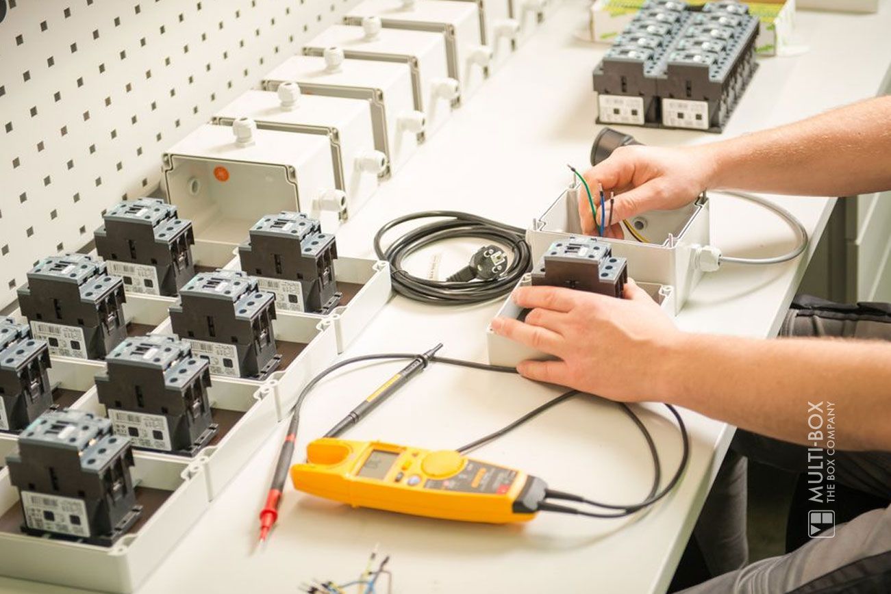 A technician wiring switch cabinets with a multimeter and multiple cables on a workbench.